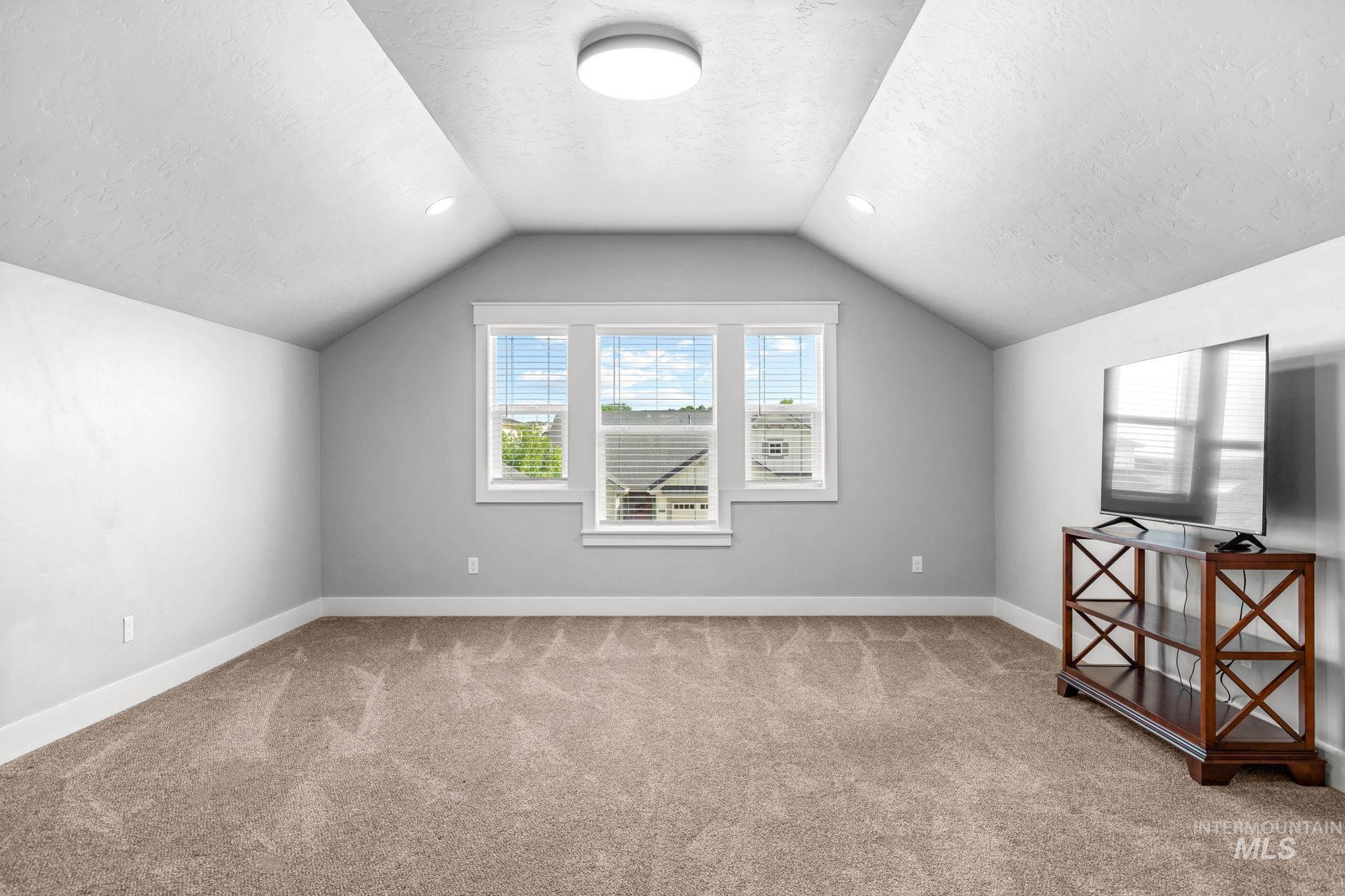 2934 East Murchison Street Meridian, ID 83642 - Photo 34 of 44 Spacious room featuring vaulted ceilings, a central window with white blinds, recessed lighting, a modern flush mount light fixture, and neutral-toned carpeting