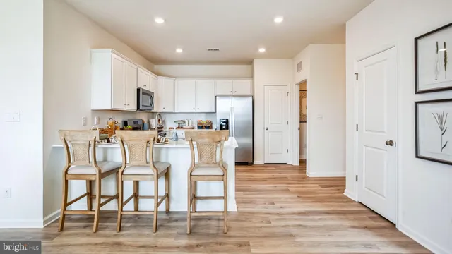 a kitchen with stainless steel appliances kitchen island granite countertop a refrigerator and a dining table cabinets wooden floor