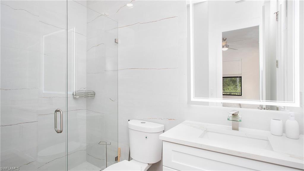 2343 Oil Well Road Naples, FL 34120 - Photo 41 of 46 Bathroom featuring a glass-enclosed shower, white marble-look wall tiling, a modern vanity with integrated sink, a rectangular illuminated mirror, and a contemporary toilet