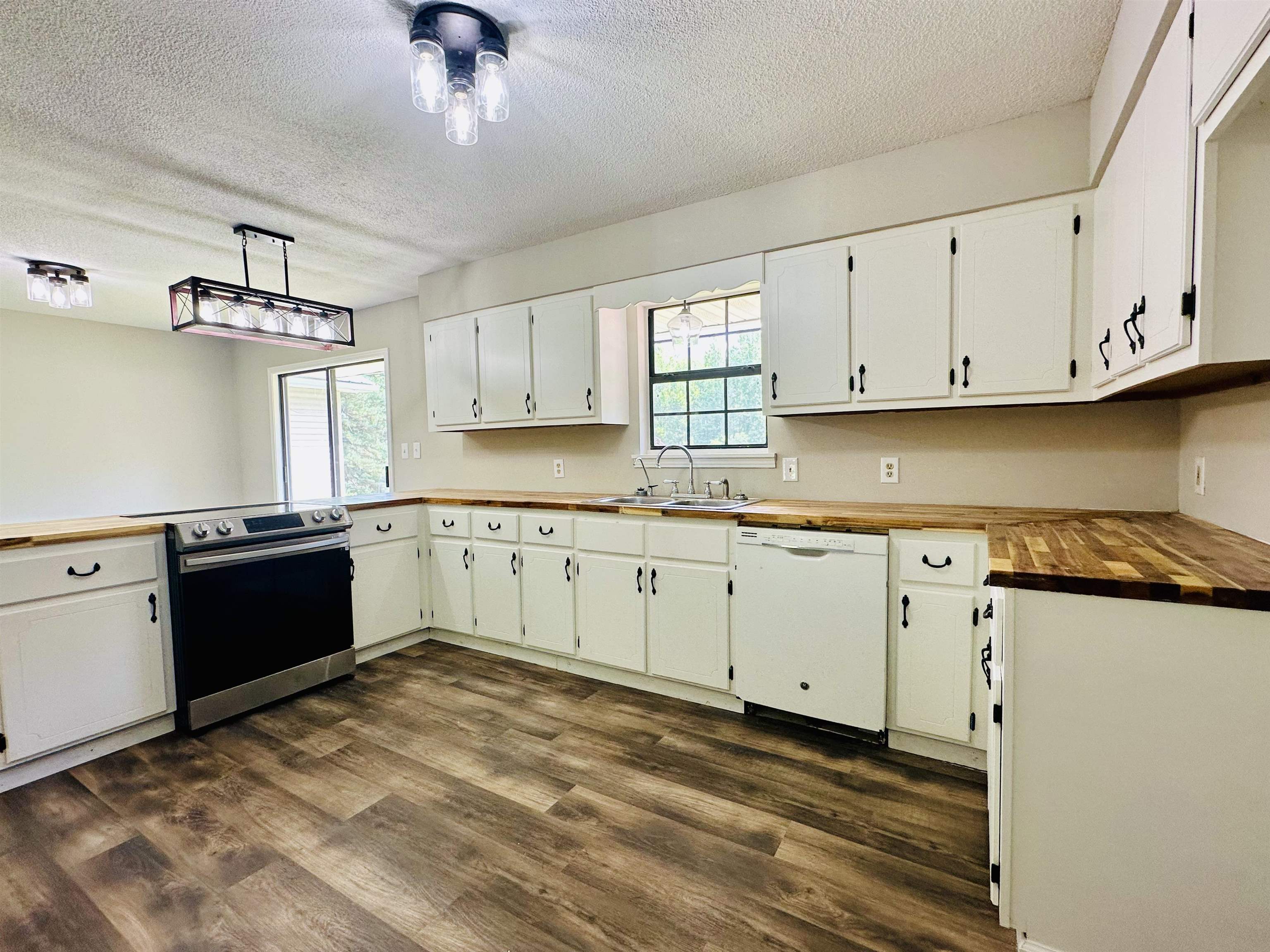 Kitchen with a textured ceiling, healthy amount of natural light, electric stove, white dishwasher, and butcher block counters