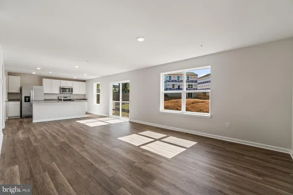 a view of an empty room with kitchen and window