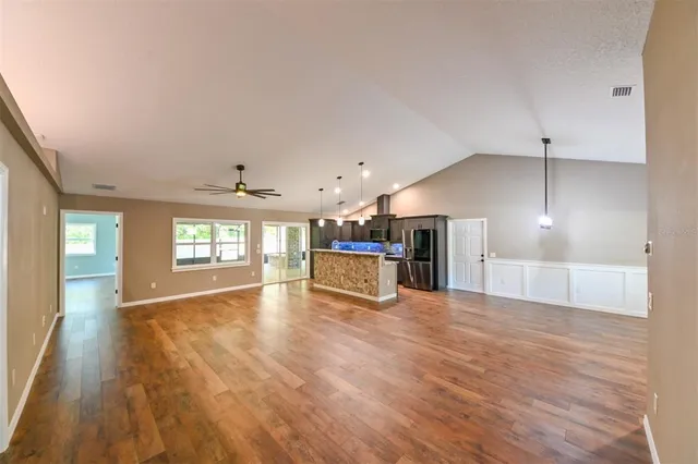 a view of an empty room with wooden floor and a kitchen