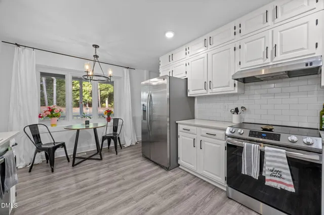 a kitchen with stainless steel appliances granite countertop a stove a refrigerator and white cabinets with wooden floors