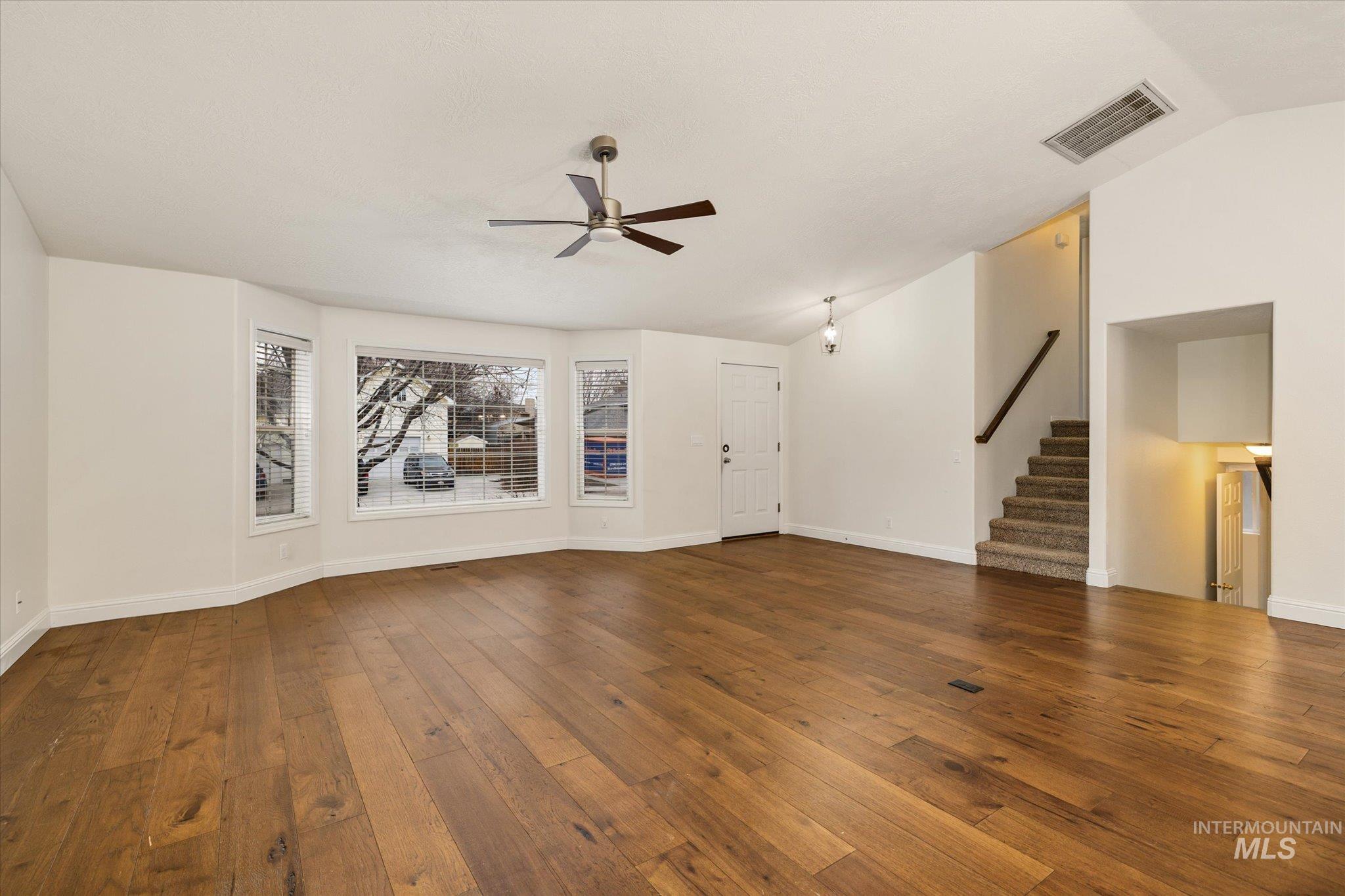 2870 North Morello Avenue Meridian, ID 83646 - Photo 3 of 20 Unfurnished living room featuring stairs, dark wood-style flooring, vaulted ceiling, and a ceiling fan