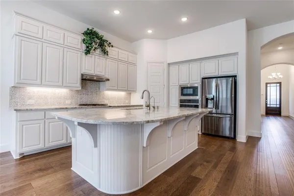 a kitchen with stainless steel appliances granite countertop a refrigerator a sink dishwasher a oven and white cabinets with wooden floor