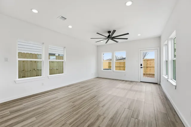 an empty room with wooden floor a ceiling fan and windows
