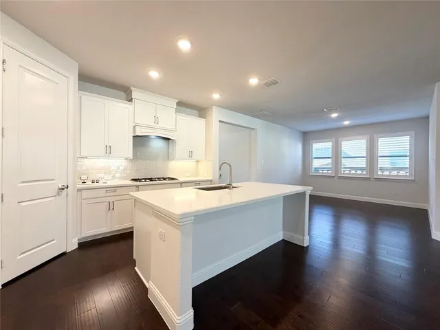 a large kitchen with granite countertop a stove top oven a sink a dishwasher and white cabinets with wooden floor