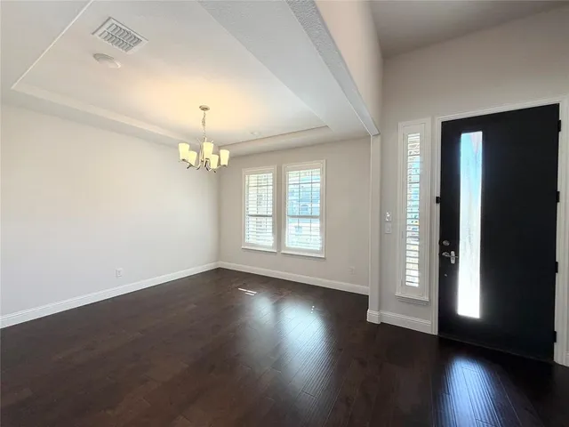 an empty room with wooden floor chandelier and windows