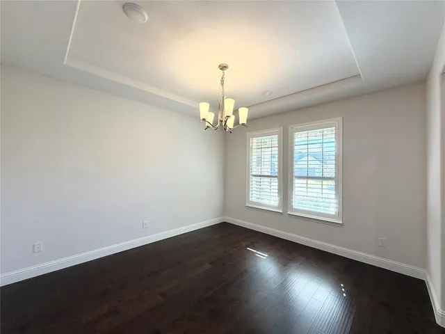 an empty room with wooden floor chandelier fan and windows
