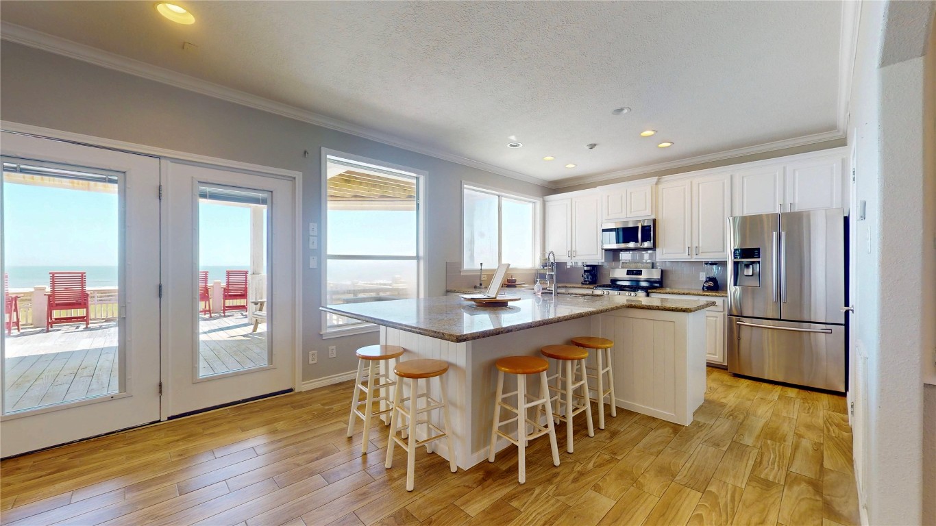 3433 Sand Castle Lane Crystal Beach, TX 77650 - Photo 21 of 30 a kitchen with stainless steel appliances granite countertop a refrigerator a stove a sink dishwasher and a dining table with wooden floor