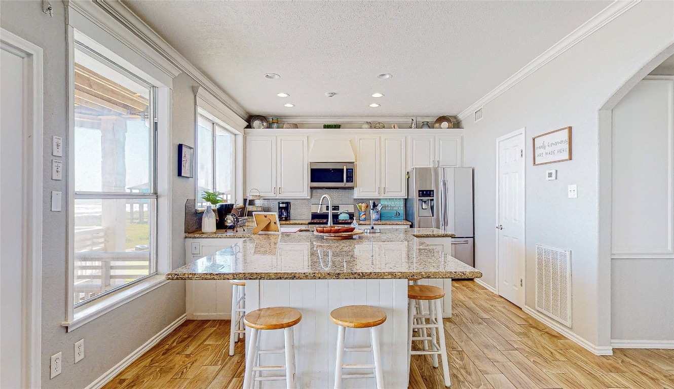 3433 Sand Castle Lane Crystal Beach, TX 77650 - Photo 9 of 30 a kitchen with stainless steel appliances granite countertop a stove top oven a refrigerator a sink and white cabinets with wooden floor