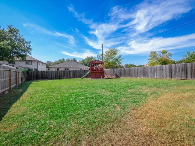 a view of back yard with grass & wooden fence