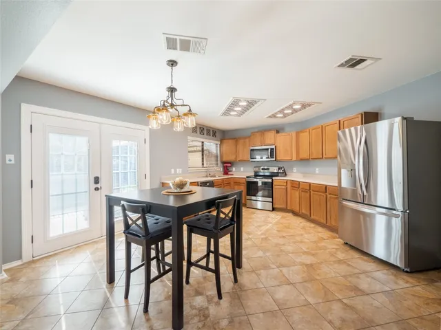 a kitchen with stainless steel appliances granite countertop a refrigerator a sink dishwasher a dining table and chairs with wooden floor