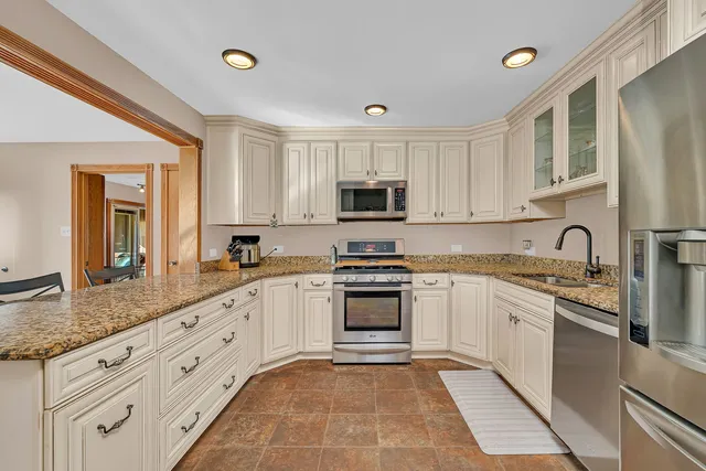 a large kitchen with stainless steel appliances granite countertop a sink and dishwasher a stove top oven with white cabinets