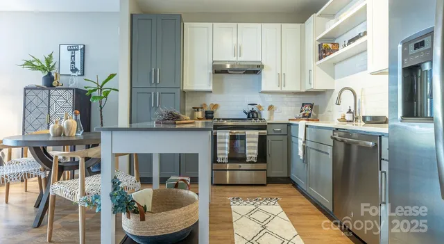 a kitchen with granite countertop a refrigerator a stove a sink and white cabinets with wooden floor