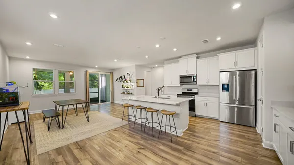 a kitchen with stainless steel appliances kitchen island granite countertop a refrigerator a stove a dining table and chairs with wooden floor