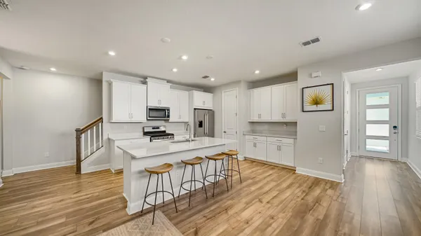 a kitchen with stainless steel appliances granite countertop a refrigerator oven stove a island and white cabinets with wooden floor
