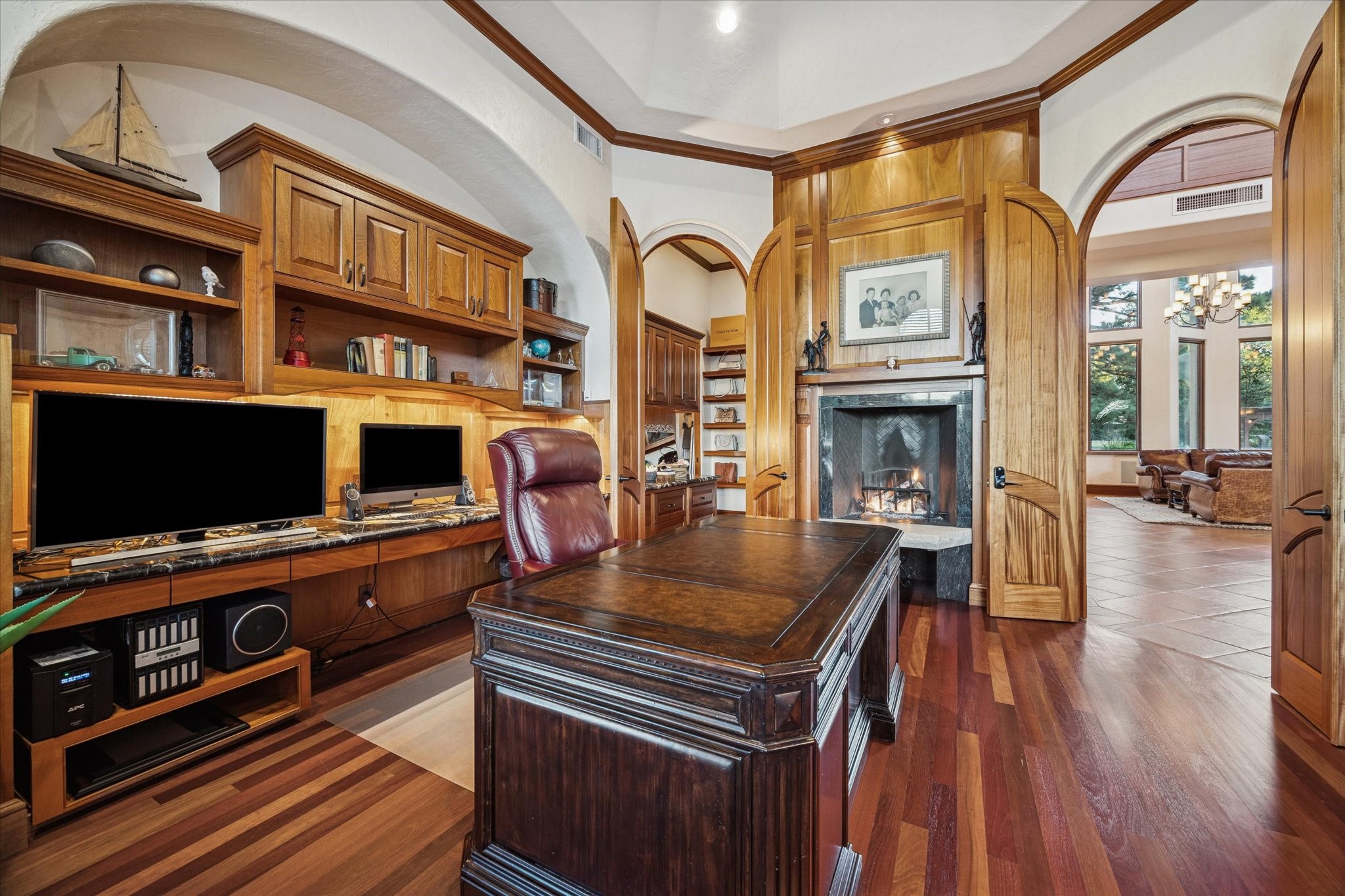 21538 Mueschke Road Tomball, TX 77377 - Photo 21 of 50 Refined main-level study. This exceptional office, viewed from another angle, showcases a stunning fireplace and beautifully crafted arched wood doors, enhancing the room’s sophisticated charm. Spacious and inviting, it offers a serene environment for work or contemplation. One of two offices in the home, this study combines luxurious design with functional elegance, perfectly complementing the home’s upscale aesthetic.