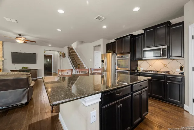 a kitchen with stainless steel appliances a refrigerator a stove a kitchen island and chairs with wooden floor