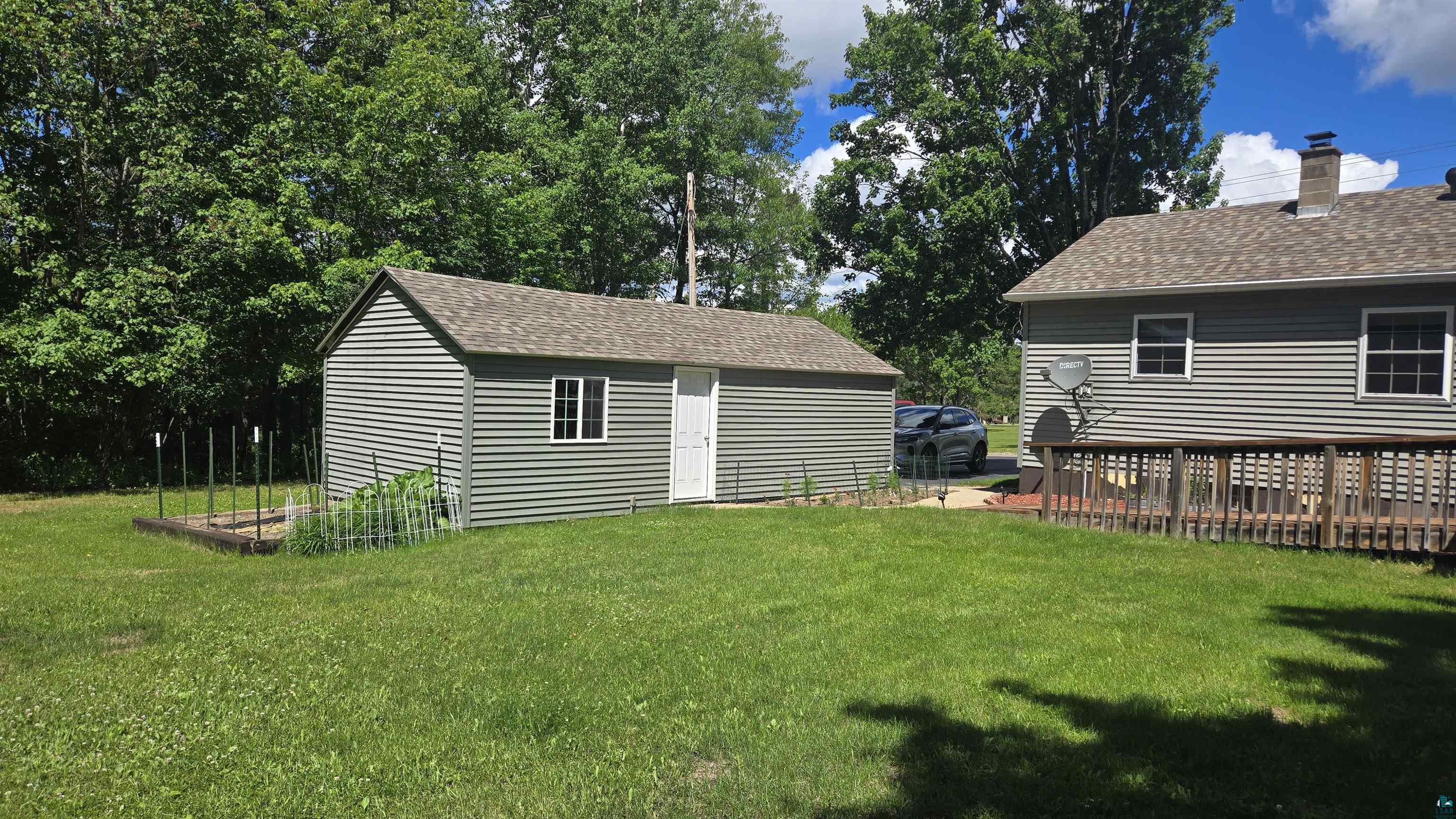 10614 Moose Lake Road Orr, MN 55771 - Photo 5 of 44 Expansive green lawn featuring a detached shed with horizontal siding, a private raised garden bed, and a sizable wood deck extending from the home