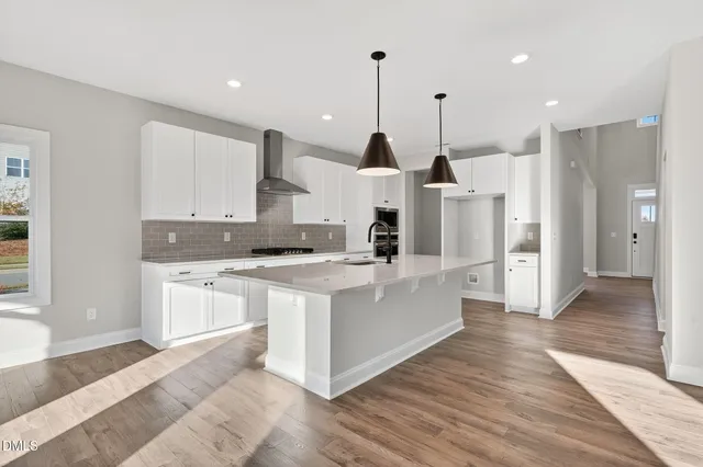 a large kitchen with stainless steel appliances kitchen island granite countertop a stove a sink a refrigerator and white cabinets with wooden floor
