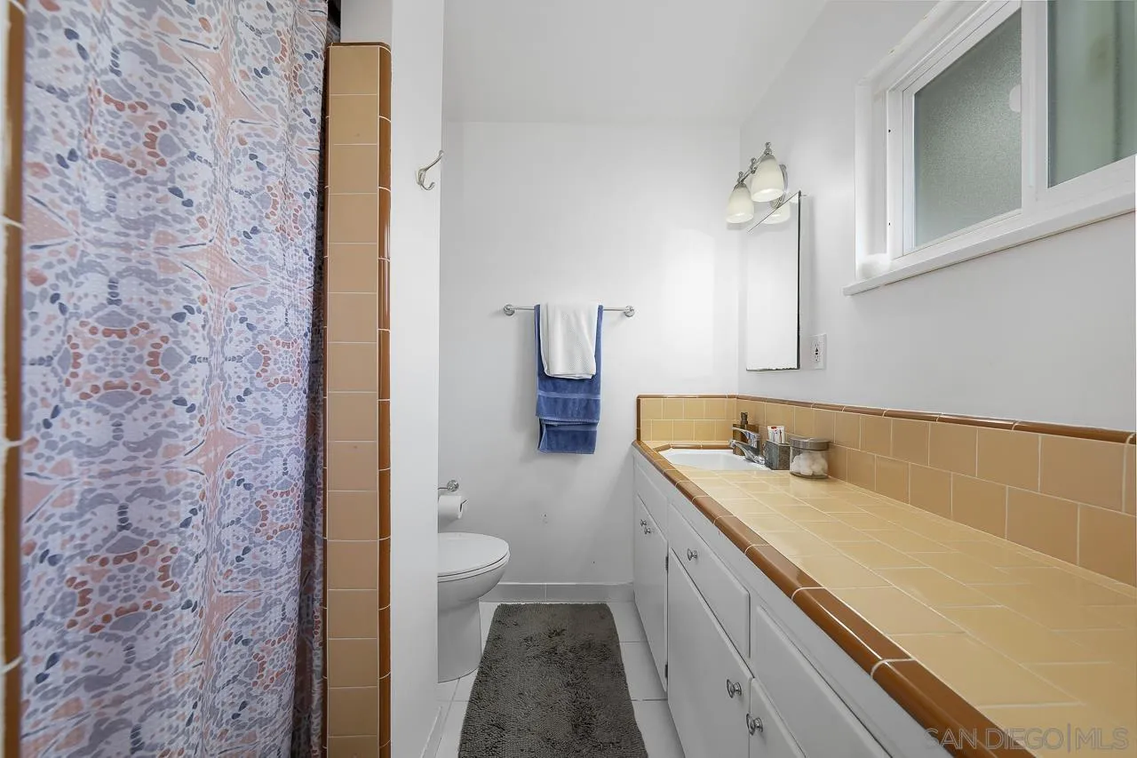 1243 Hardin Drive El Cajon, CA 92020 - Photo 21 of 32 a bathroom with a granite countertop sink a toilet and shower curtain