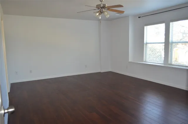 an empty room with wooden floor fan and windows