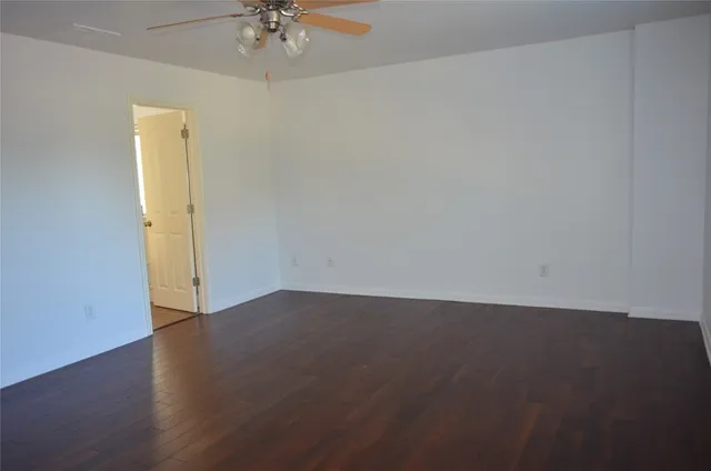 an empty room with a chandelier fan and wooden floor