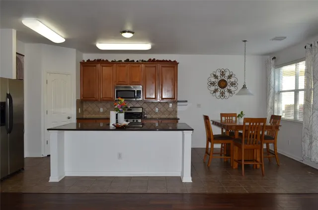 a kitchen with stainless steel appliances kitchen island granite countertop a table chairs and a refrigerator