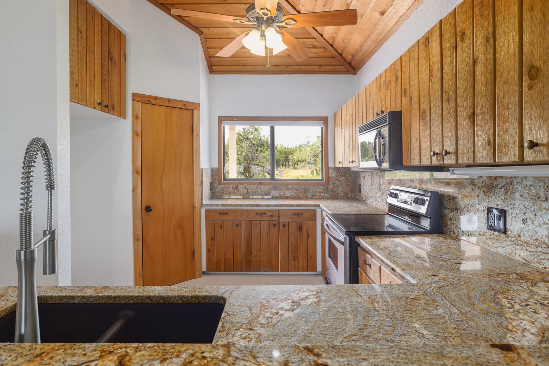 313 Kendall Road Spicewood, TX 78669 - Photo 9 of 34 Kitchen with wood ceiling, stainless steel electric range, brown cabinetry, tasteful backsplash, and black microwave