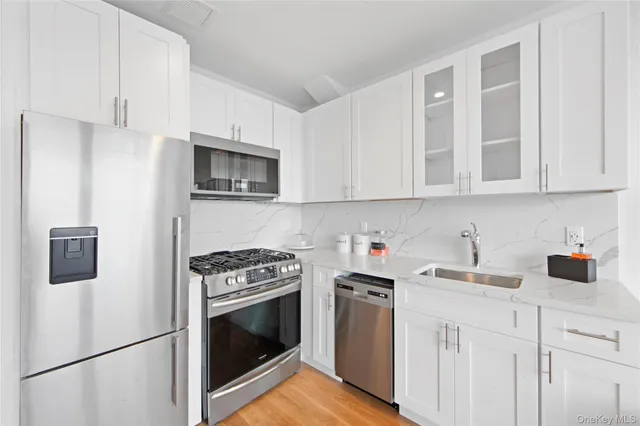 a kitchen with stainless steel appliances granite countertop white cabinets a stove a refrigerator a sink and dishwasher with wooden floor