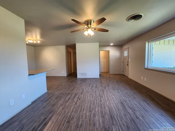 a view of an empty room with wooden floor and a ceiling fan