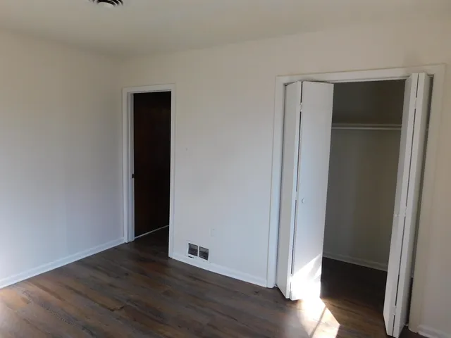 a view of an empty room with wooden floor and closet