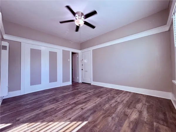 a view of an empty room with wooden floor and a ceiling fan