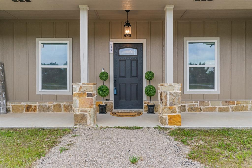 139 Kriston Lane Springtown, TX 76082 - Photo 4 of 39 Front entry featuring a dark paneled door with an arched glass insert, flanked by two white-framed windows