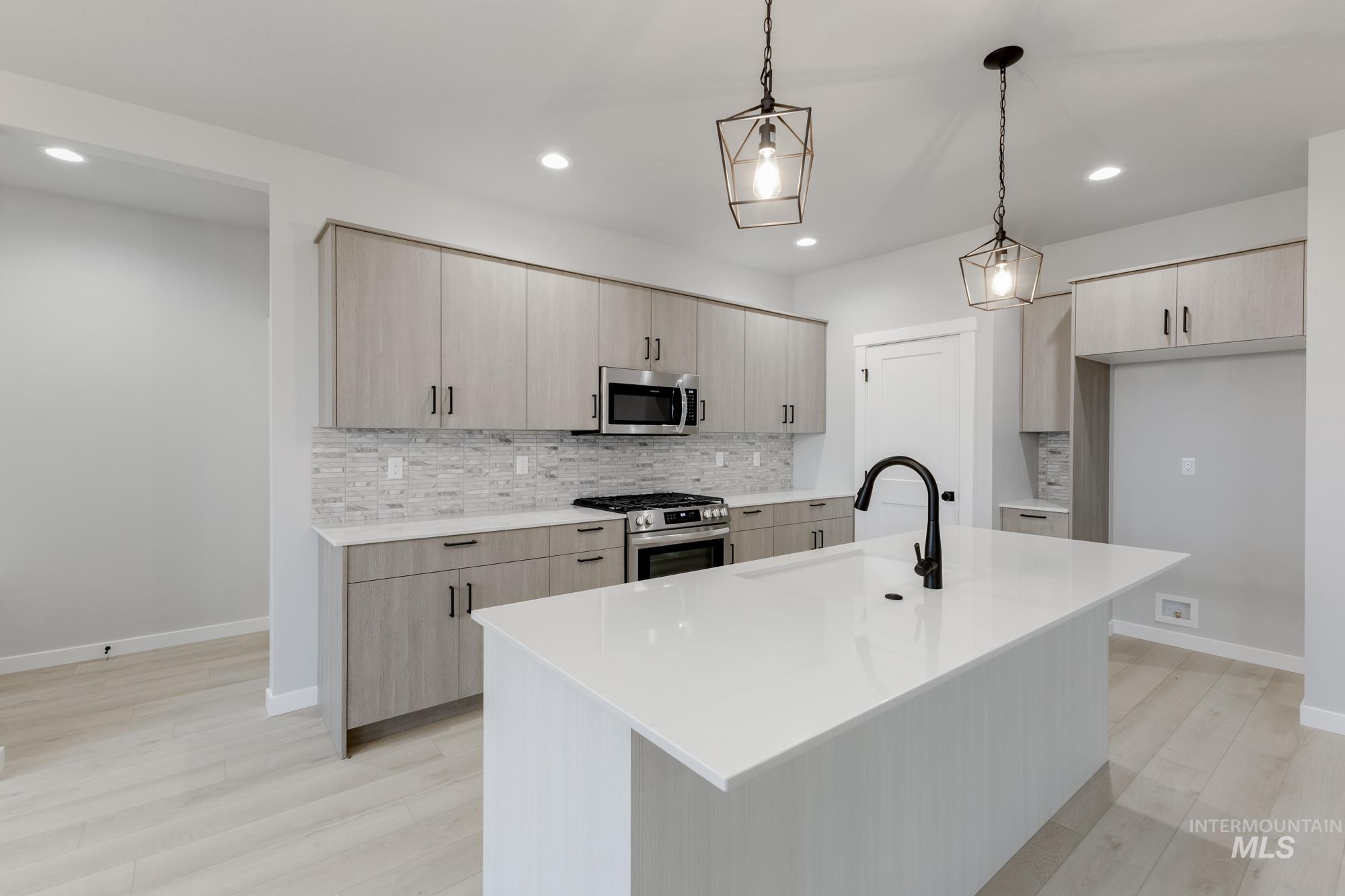 6494 South Sunfish Avenue Boise, ID 83709 - Photo 5 of 32 Kitchen with decorative backsplash, light brown cabinetry, an island with sink, hanging light fixtures, and light stone countertops
