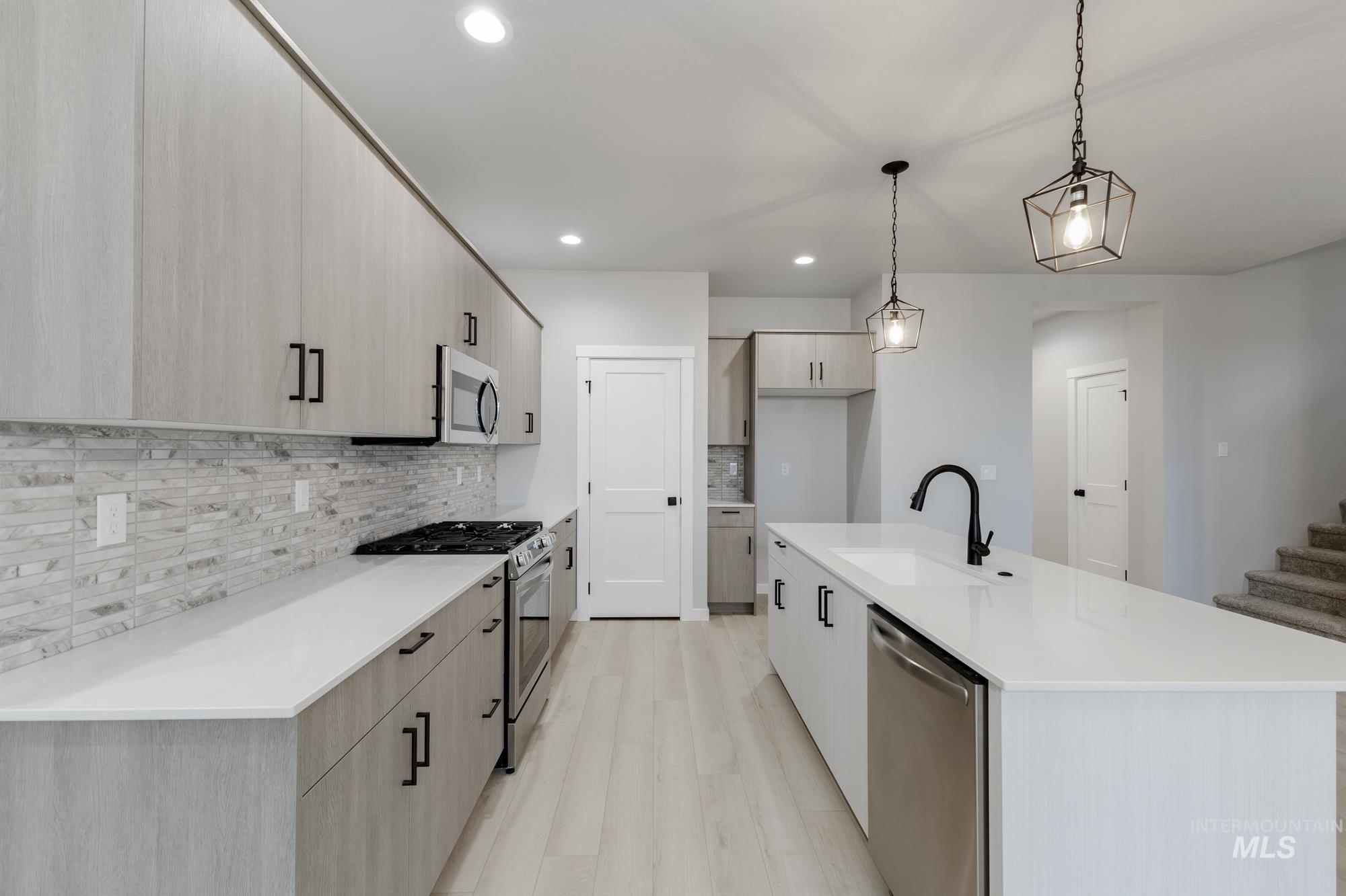 6494 South Sunfish Avenue Boise, ID 83709 - Photo 6 of 32 Kitchen with stainless steel appliances, decorative backsplash, decorative light fixtures, a center island with sink, and light stone counters