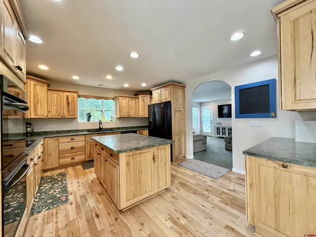 a kitchen with stainless steel appliances granite countertop a stove top oven a sink dishwasher a refrigerator and white cabinets with wooden floor