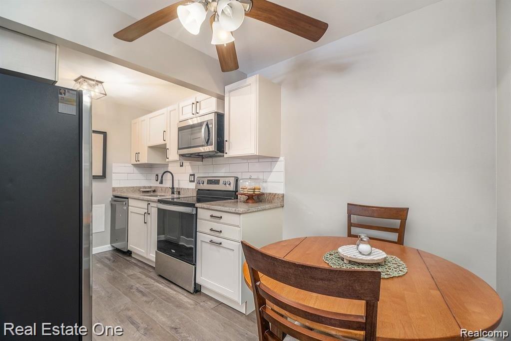 803 Plate Street, Unit 104 Rochester, MI 48307 - Photo 12 of 14 Kitchen space featuring white cabinetry, subway tile backsplash, stainless steel appliances, wood-finish flooring, and a ceiling fan with integrated lighting