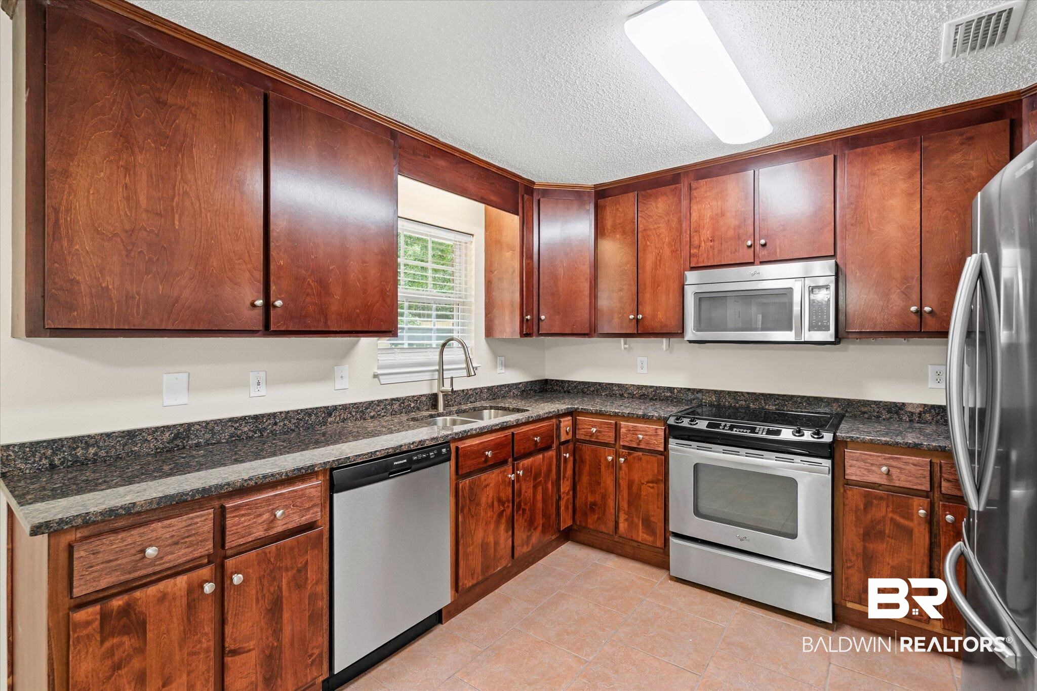 157 Bay View Drive Daphne, AL 36526 - Photo 6 of 22 Kitchen with appliances with stainless steel finishes, dark stone counters, a textured ceiling, and light tile patterned flooring