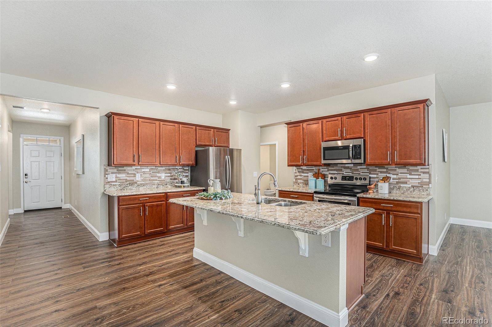 1051 Draw Street Brighton, CO 80603 - Photo 8 of 19 a kitchen with stainless steel appliances granite countertop a stove top oven a sink dishwasher a refrigerator and a dining table with wooden floor