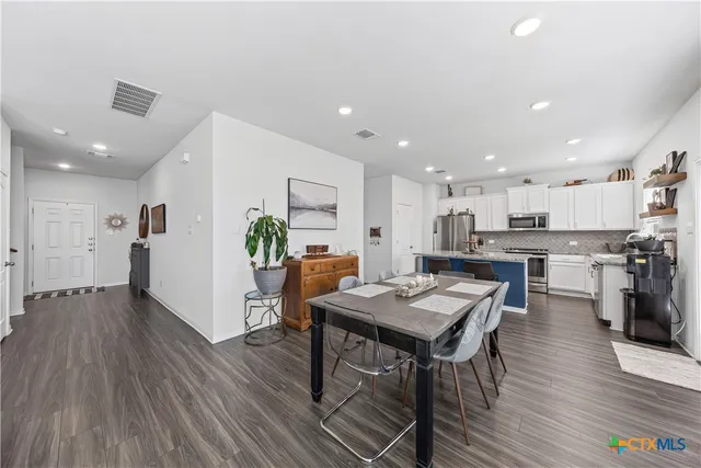 a living room with stainless steel appliances furniture wooden floor and a kitchen view