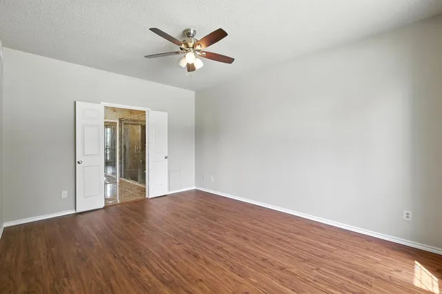 a view of an empty room with wooden floor and a ceiling fan
