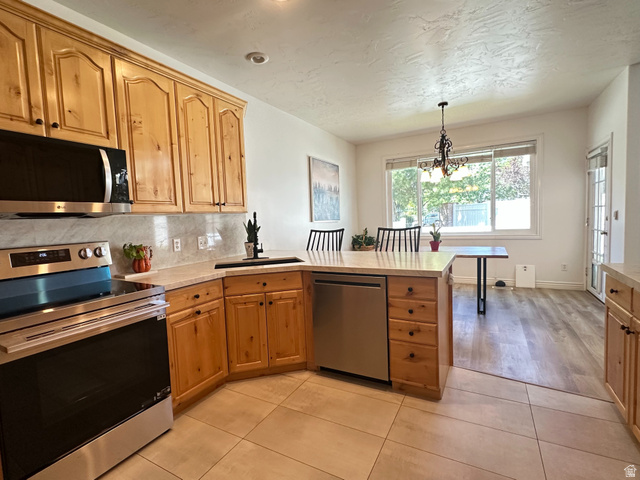 Kitchen featuring wood-finish cabinetry, stainless steel appliances, light-toned countertops, and a tile backsplash