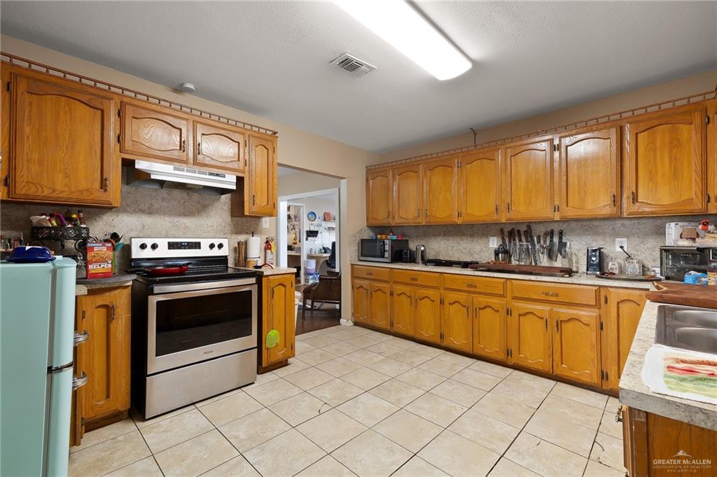 3721 North Veterans Boulevard Pharr, TX 78577 - Photo 9 of 18 Kitchen featuring tasteful backsplash, appliances with stainless steel finishes, brown cabinetry, under cabinet range hood, and visible vents