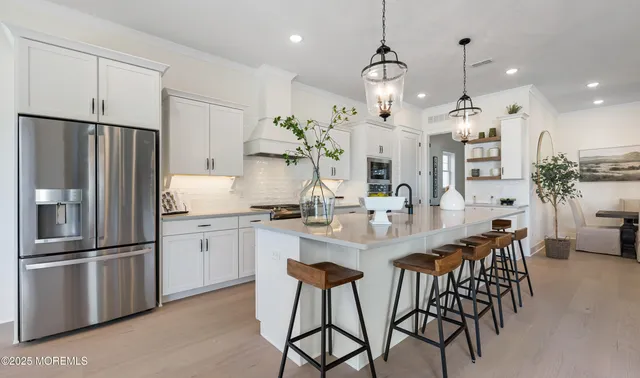 a kitchen with stainless steel appliances granite countertop a refrigerator a sink dishwasher a dining table and chairs with wooden floor