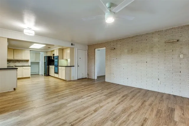 a view of an empty room with wooden floor and a kitchen