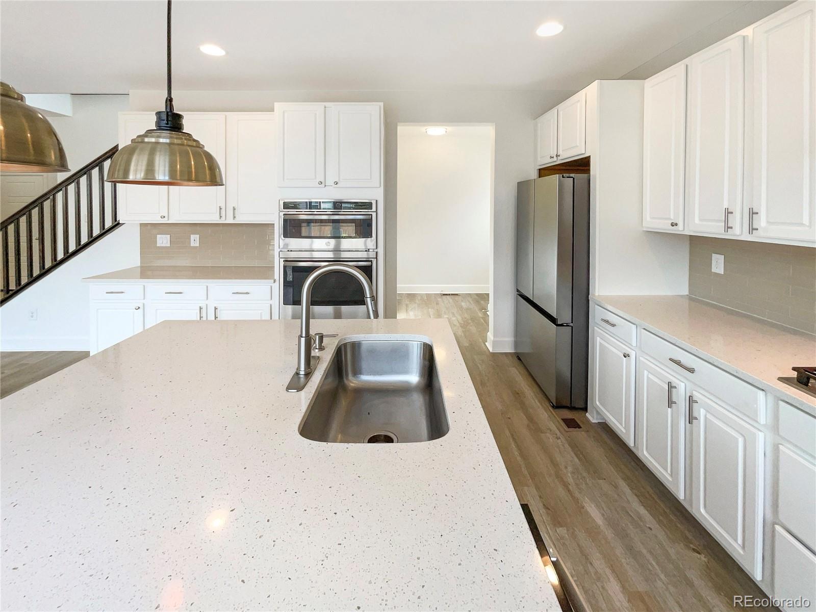 27895 East 7th Place Aurora, CO 80018 - Photo 6 of 35 a kitchen with kitchen island granite countertop a sink a counter and a refrigerator