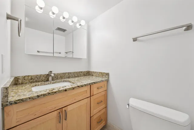 a bathroom with a granite countertop sink a toilet and mirror