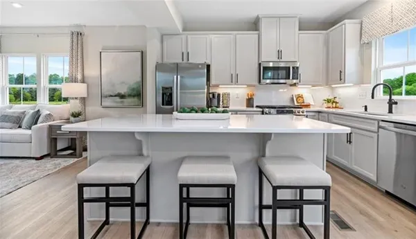 a white kitchen with stainless steel appliances a table chairs refrigerator and microwave